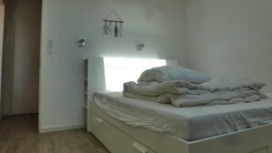 Ein schlicht eingerichtetes Schlafzimmer mit einem Bett, einem kleinen Nachttisch und einer Wandleuchte.