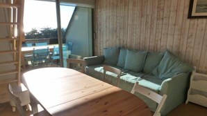 Ein Zimmer mit einem Holztisch, einem grünen Sofa mit Kissen und einer Schiebeglastür zu einem Außenbereich.