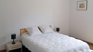 Une chambre à coucher au style minimaliste, avec un grand lit, une tête de lit en bois, du linge de lit blanc, une table de chevet avec une lampe et un luminaire suspendu.