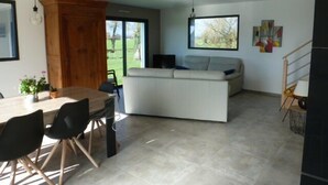 A modern living room with a sofa, a dining table with chairs, and a wooden cabinet. - Maison 8 personnes, la mer et la campagne (AMBON)