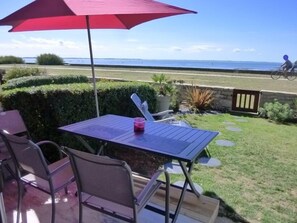 An outdoor patio with a table and chairs, a red umbrella, and a view of the sea. - Very nice ground floor apartment with sea view (DAMGAN)