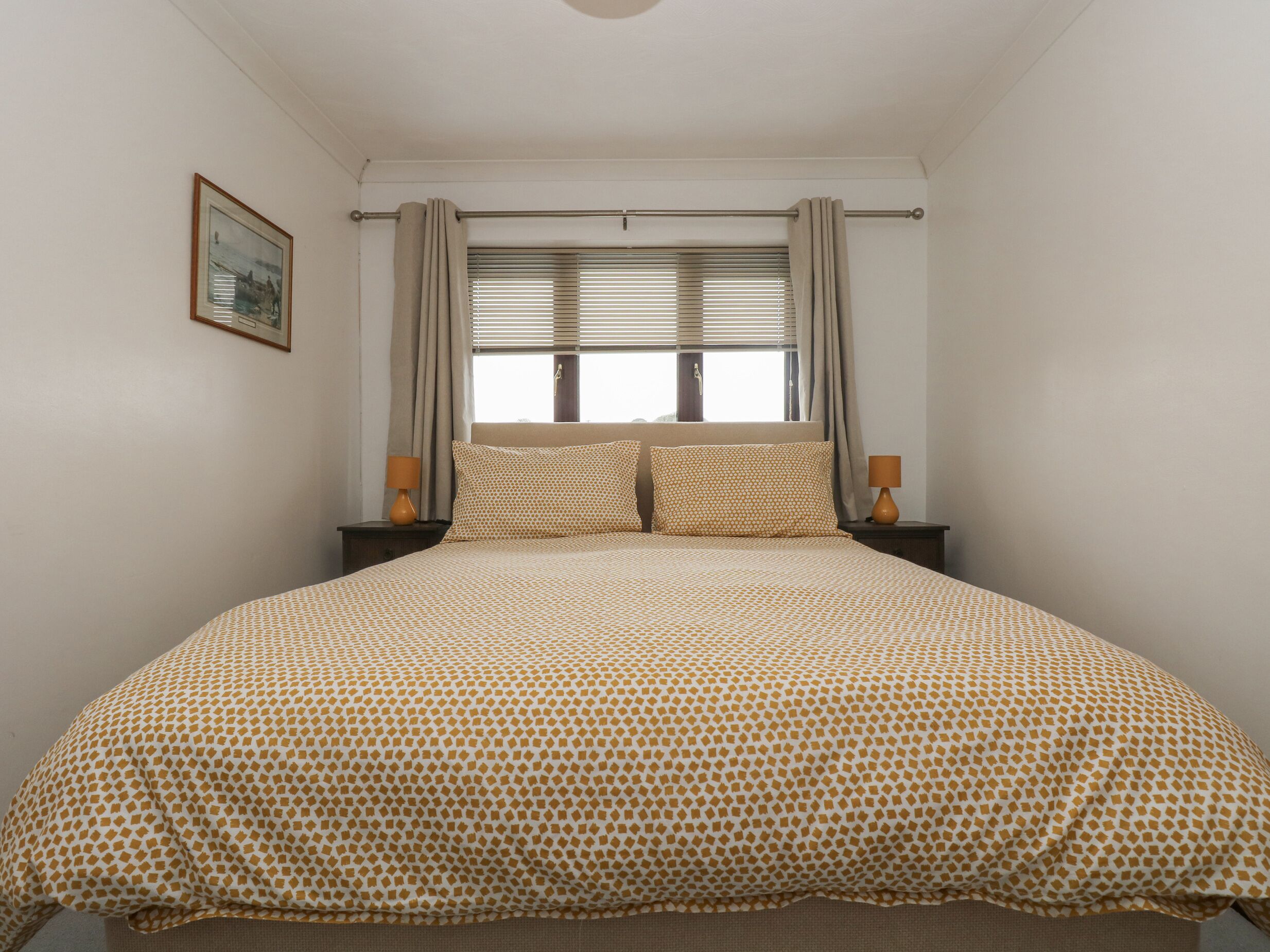 A bedroom with a bed, two bedside tables, a window with blinds, and a picture on the wall.