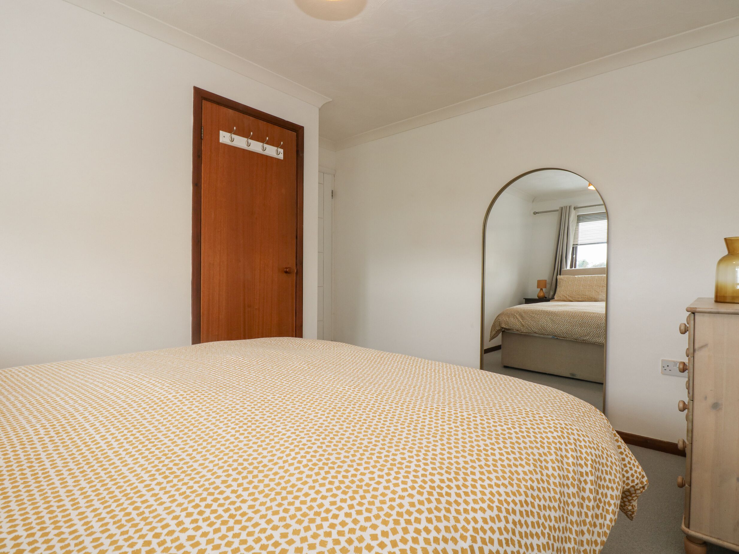 A bedroom with a bed, a wooden wardrobe, a door with a sign, and a mirror reflecting a bed and window.