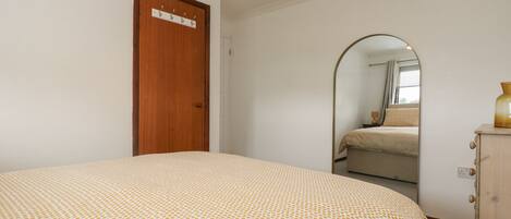 A bedroom with a bed, a wooden wardrobe, a door with a sign, and a mirror reflecting a bed and window.