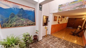Eine Hotelhalle mit einer großen Wandmalerei von Machu Picchu, Zimmerpflanzen, einem Holzstuhl und einem gefliesten Boden.