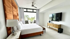Ein modernes Hotelzimmer mit einem großen Bett, einem Fernseher, einer Holzkredenz und einem Balkon mit Sitzgelegenheit im Freien.