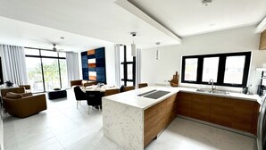 Eine moderne Küche mit Kochinsel, ein Essbereich mit Aussicht und ein Wohnbereich mit Sofa und Couchtisch.