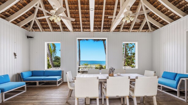 A covered outdoor seating area with white walls, wooden flooring, and a thatched roof. - Waterfront House located in Schooner Bay, Abaco (Crossing Rocks)