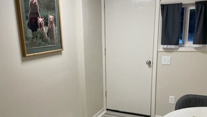 Ein Zimmer mit weißer Tür, einem gerahmten Bild an der Wand, einem runden Tisch mit Untersetzer und einem gemusterten Teppich auf dem Boden.