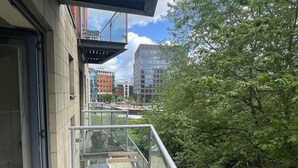 A balcony with a glass railing, wooden deck, and a view of urban buildings and trees. - Remarkable 2-bed Apartment in Leeds (Leeds)