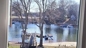 A view through a window of a river with boats, a wooden dock, and leafless trees.