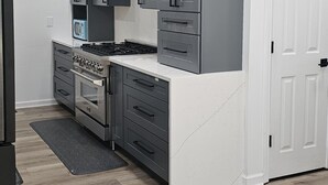 A modern kitchen with grey cabinets, a white countertop, and a stainless steel stove.