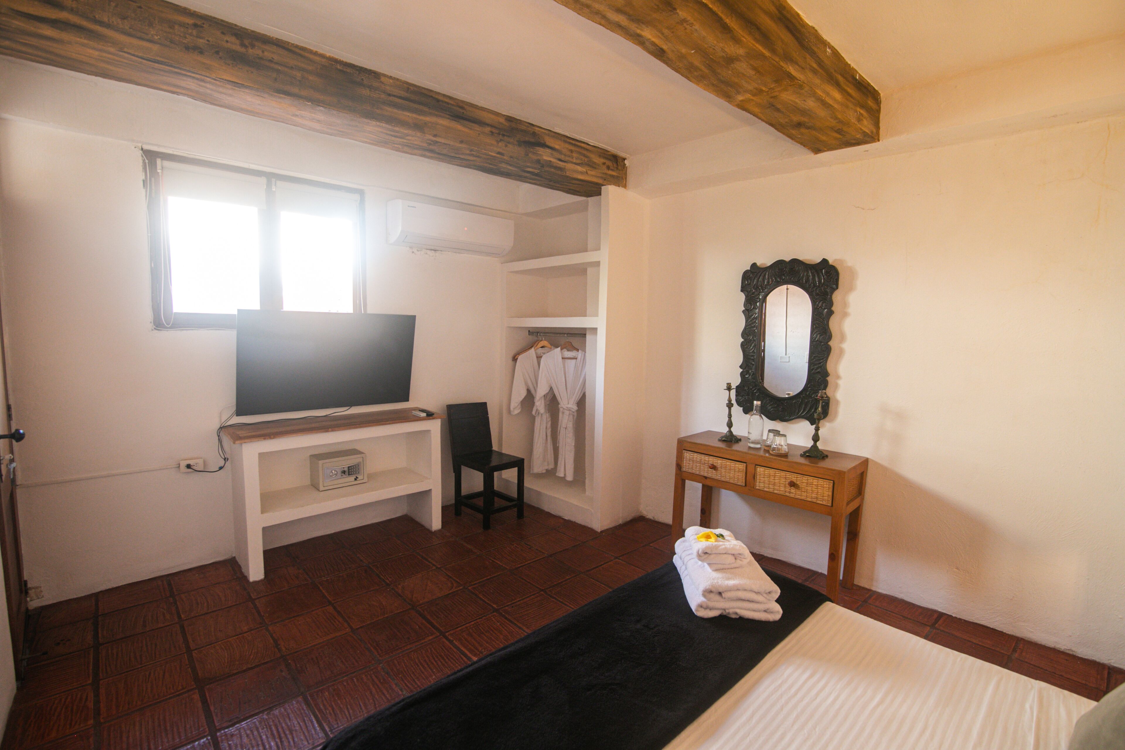Un dormitorio con cama, televisión, cómoda de madera, espejo y ventana.