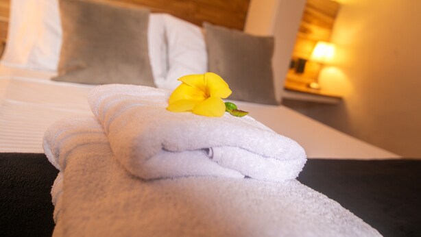 A neatly made bed with white and gray linens, a yellow flower, and a wooden headboard. - Casa Be Getsemani (Cartagena)