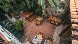 An outdoor patio area with wooden tables and chairs, surrounded by lush tropical plants and a stone wall. - Casa Be Getsemani (Cartagena)