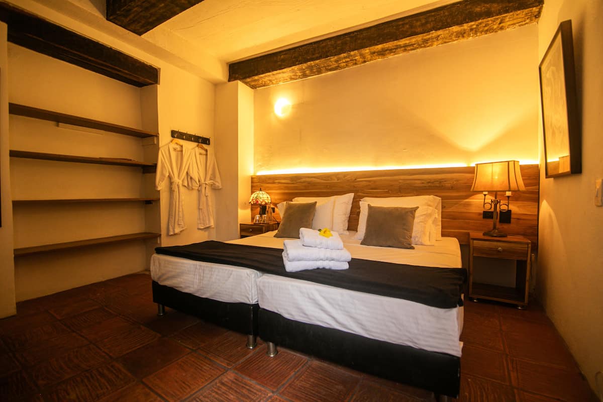 A hotel room with a double bed, a bedside table with a lamp, a wooden headboard, and a wall-mounted towel rack.