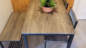 Una mesa de comedor de madera con una maceta rosa de plantas verdes en el centro, rodeada por cuatro sillas con estructura de metal negro.