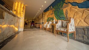 A lobby with a marble reception desk, a mural depicting a historical scene, and ornate seating. - King Pyramids View Hotel (Giza)