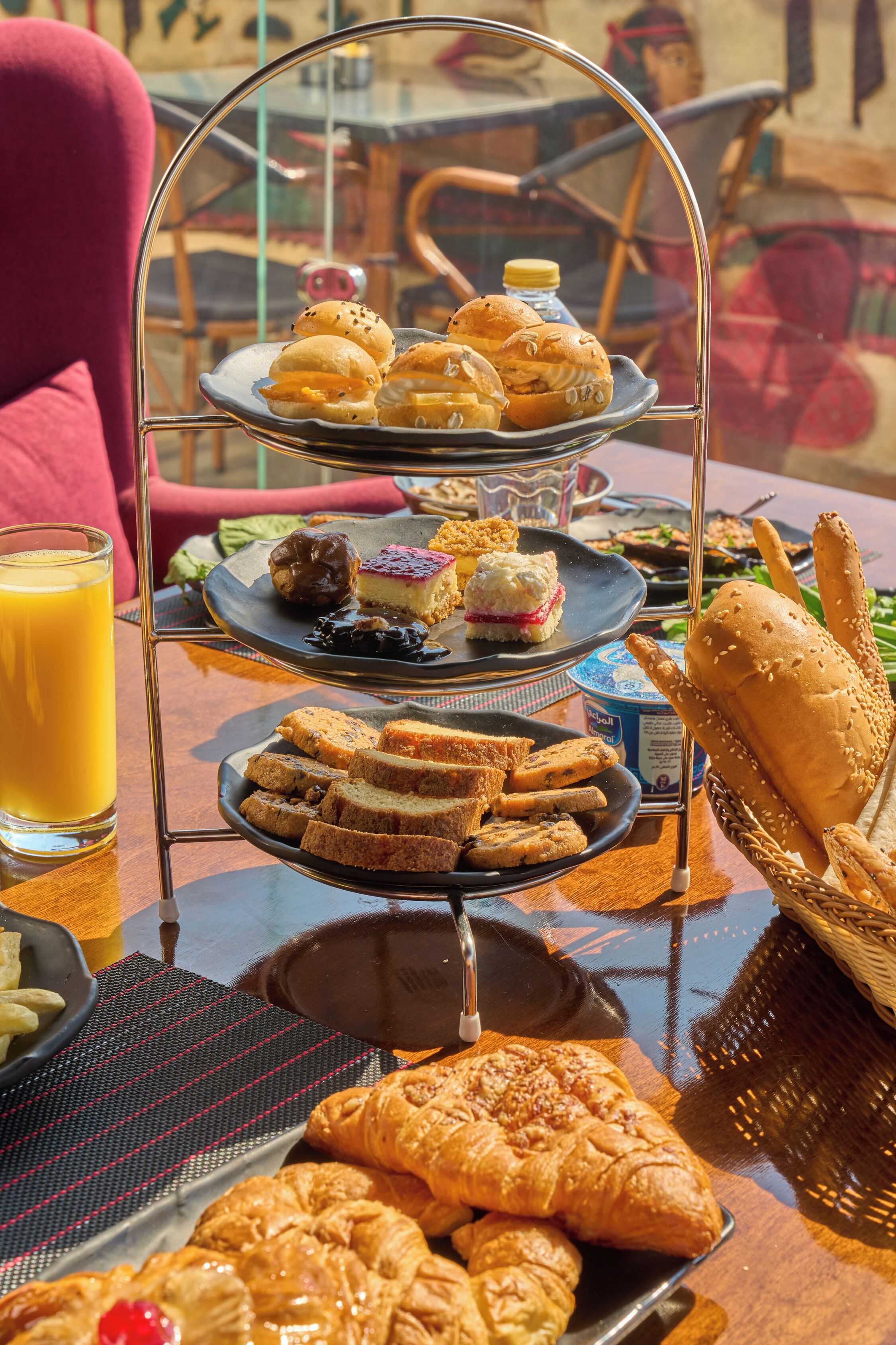 A tiered tray with pastries, sandwiches, and a glass of orange juice on a table.
