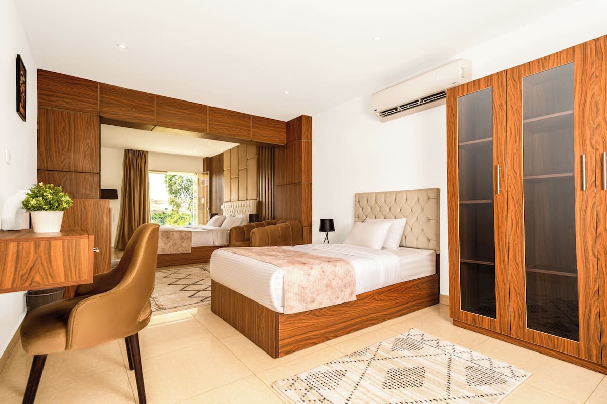 A modern bedroom with a large bed, a desk, a chair, and a wardrobe.