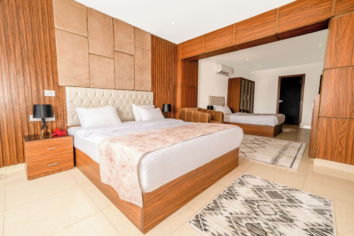 A modern bedroom with a large bed, wooden paneling, a built-in wardrobe, and a separate seating area.