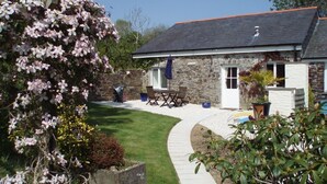 A stone house with a white door, a paved patio, and a garden with flowering plants. - Beautiful 4* Cottage in a peaceful, rural setting with Country Club membership.  (Saltash)