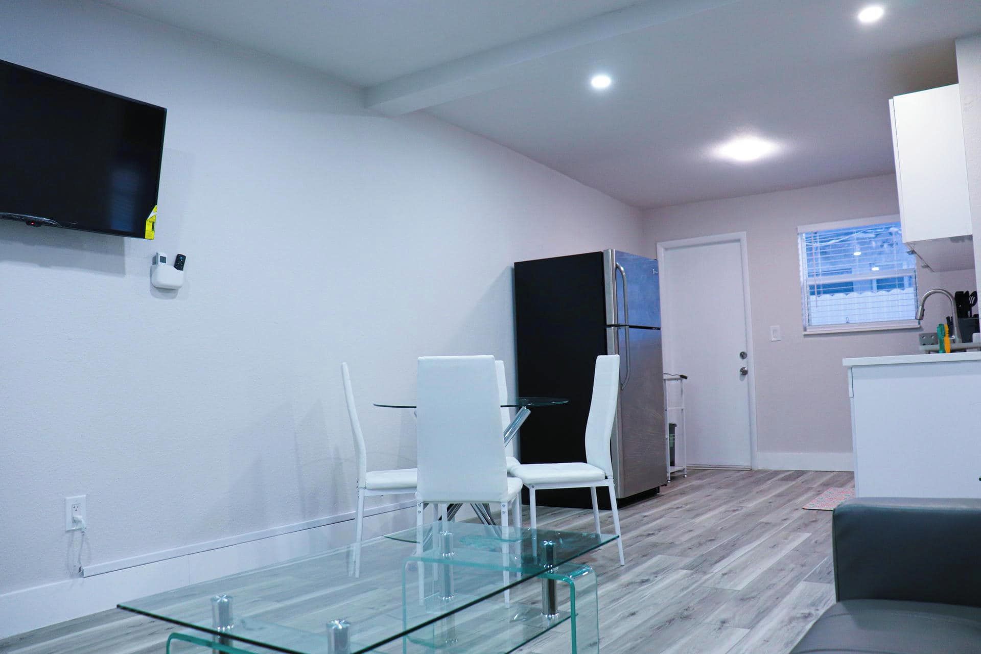 A modern kitchen with a refrigerator, a dining table with chairs, and a TV mounted on the wall.