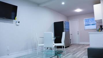 A modern kitchen with a refrigerator, a dining table with chairs, and a TV mounted on the wall.