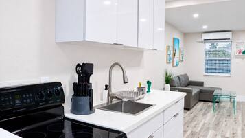 Una cocina moderna con estufa negra, gabinetes blancos y un lavamanos de acero inoxidable.