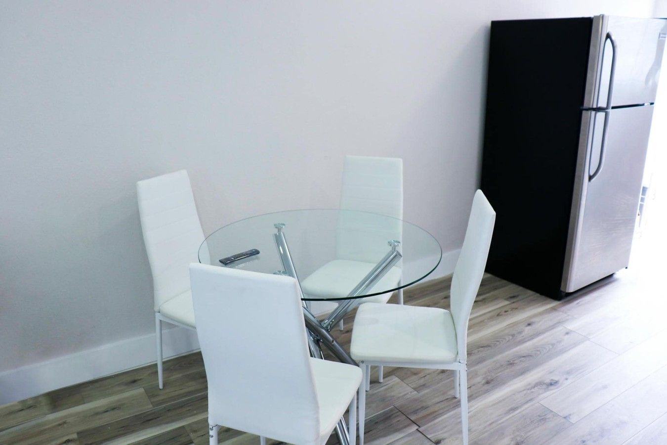 A modern kitchen with a round glass table, white chairs, and a black refrigerator.