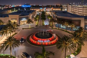Un carrefour giratoire avec une fontaine au centre, entouré de palmiers et d’immeubles dont les enseignes sont illuminées.