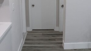 Un couloir avec un plancher en bois, des murs blancs et une porte fermée au bout.
