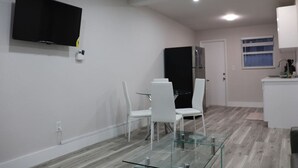 Une cuisine moderne avec des meubles blancs, un réfrigérateur noir et une table à manger en verre, assortie de chaises blanches.