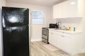 A kitchen with white cabinets, a black refrigerator, an oven, and a window.