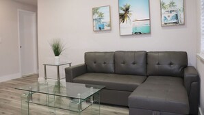 Un salon avec un canapé gris, une table basse en verre et des œuvres d’art murales représentant une scène de plage.