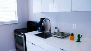 Une cuisine de taille réduite, équipée d’une cuisinière, d’un évier et de meubles blancs.