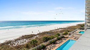 Vista sulla spiaggia dal balcone di un hotel, con piscina e lettini.
