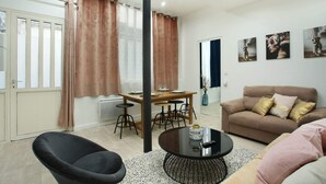 Una sala de estar moderna con un sofá, una mesa redonda de centro, una mesa de comedor con sillas y una butaca negra.
