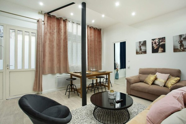 A modern living room with a sofa, a round coffee table, a dining table with chairs, and a black chair.