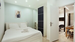 Un dormitorio moderno con cama, armario y zona de comedor visible a través de una puerta abierta.