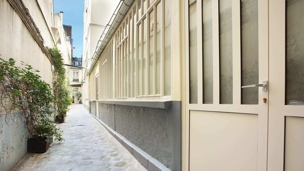 Un estrecho callejón empedrado con un edificio a un lado, que tiene ventanas grandes y una puerta.