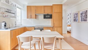 Een moderne keuken met houten kastjes, een inbouwoven en een eethoek met een tafel en stoelen.