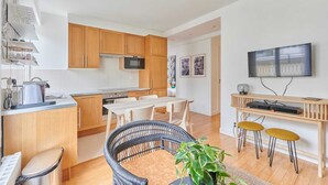 Een compacte keuken met houten kastjes, een eettafel en een aan de muur bevestigde televisie.