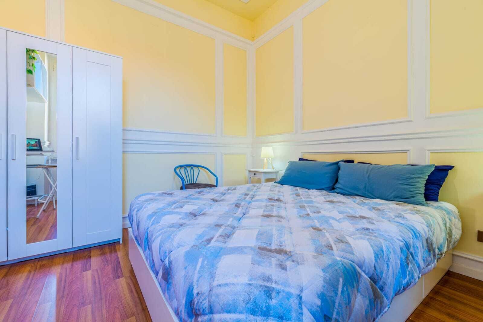 A bedroom with a bed, a chair, a wardrobe, and a nightstand.