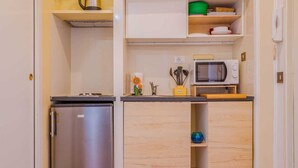 Eine kleine Küchenzeile mit einem Edelstahlkühlschrank, einer Mikrowelle und Holzschränken.