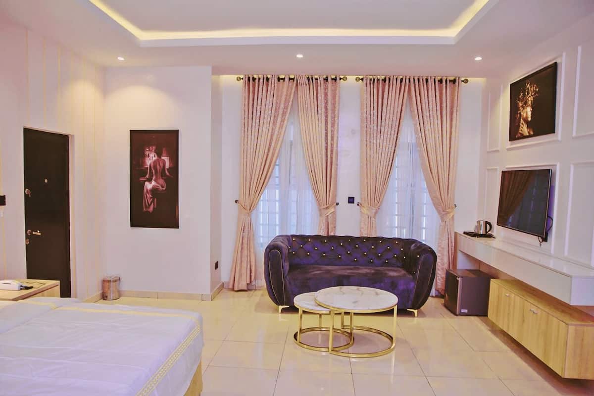 A modern hotel room with a large bed, a round coffee table, a sofa, and a TV.