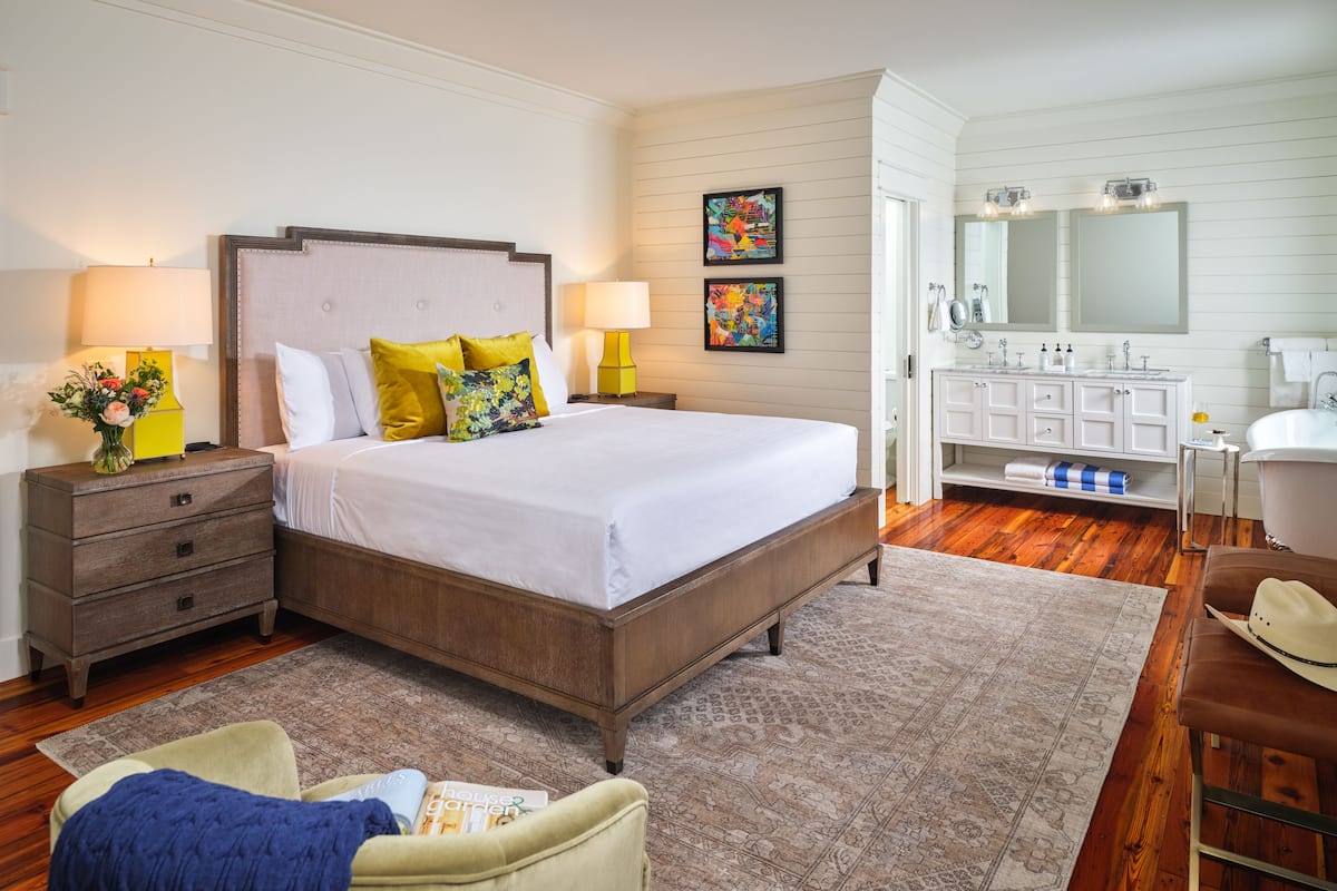Un dormitorio con una cama grande, mesitas de noche, un aparador, un espejo y un baño con lavabo y espejo.