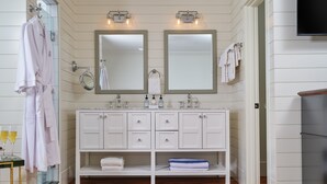 Un baño con suelo de madera, tocador blanco con dos espejos y cabina de ducha de vidrio.