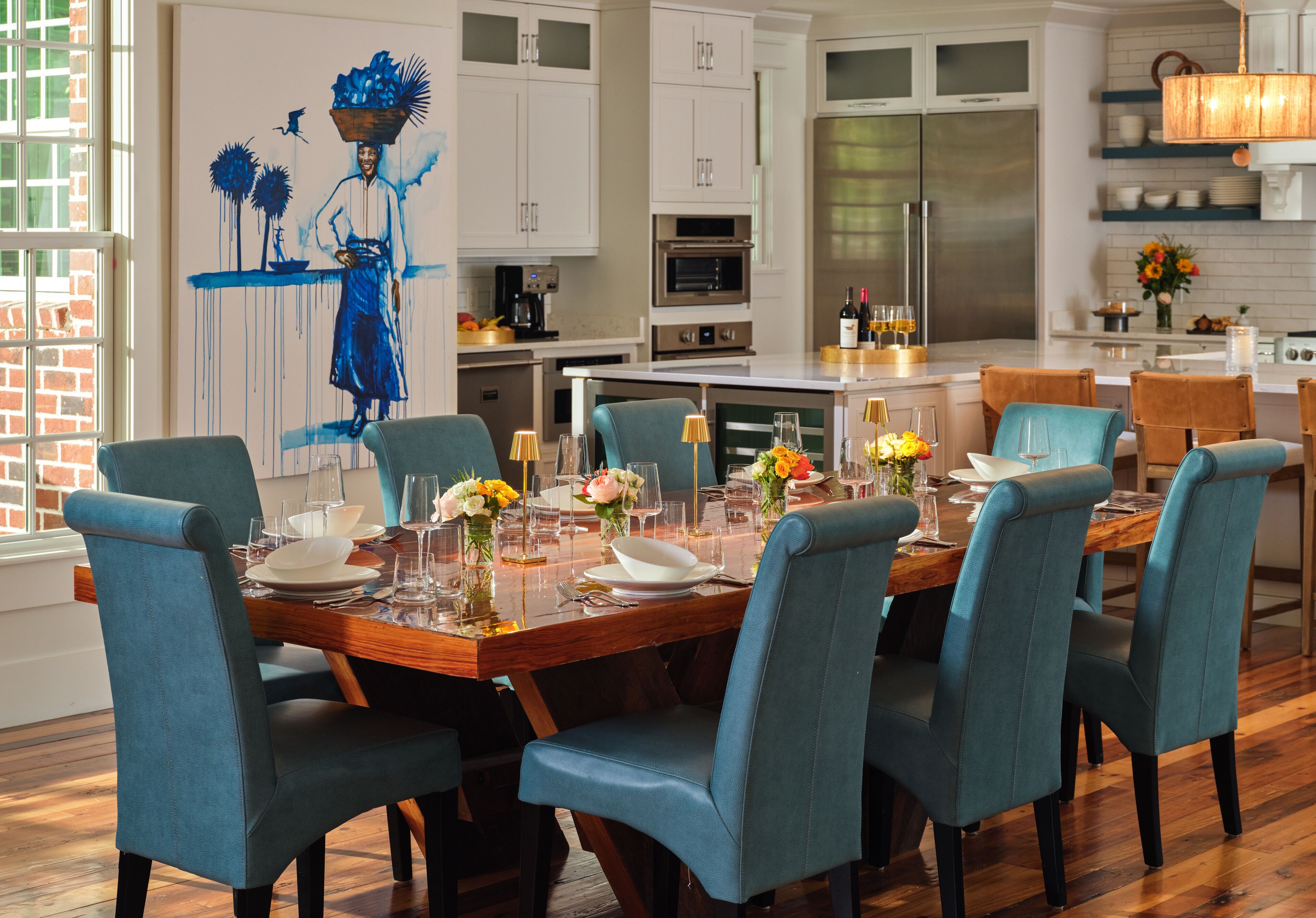 Een moderne keuken met witte kasten, roestvrijstalen apparatuur, en een eethoek met blauwe stoelen en een houten tafel gedekt voor zes personen.