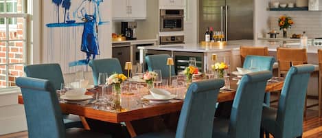 A modern kitchen with white cabinets, stainless steel appliances, and a dining area with blue chairs and a wooden table set for six.
